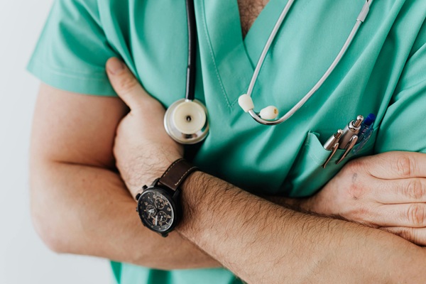 Picture of male doctor's arms and part of his chest wearing scrubs, a watch and a stethoscope.