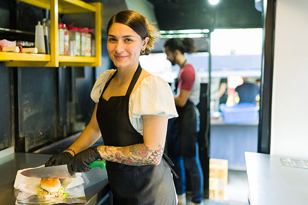 female food truck owner cutting sandwich inside food truck