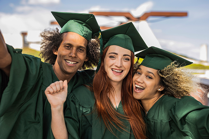 Three graduates wearing green caps and gowns cheer