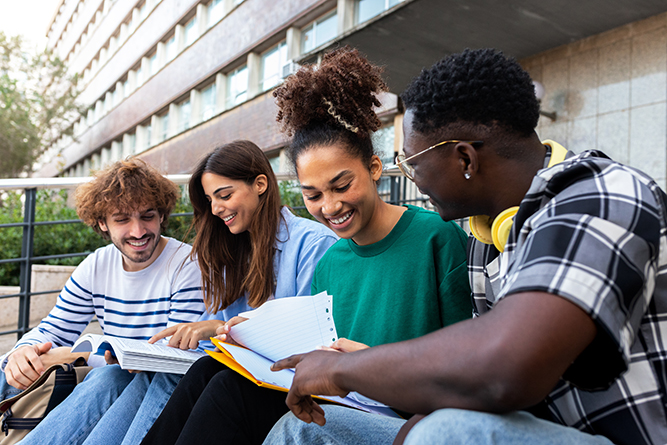 A group of four older students sitting down review papers and a textbook